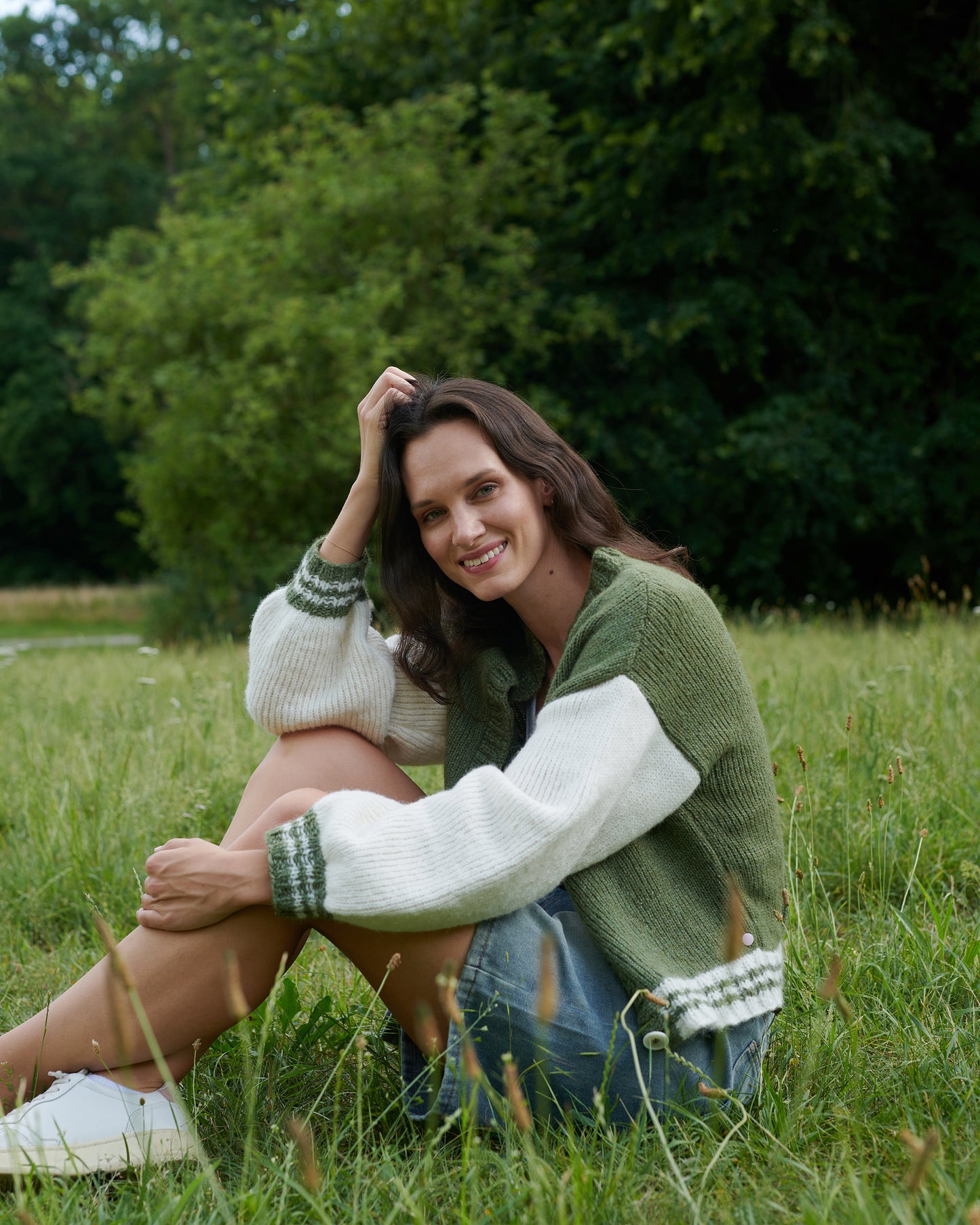 Alpaka College Cardigan VIVIAN an Model im Gras sitzend in der Farbe natur oregano