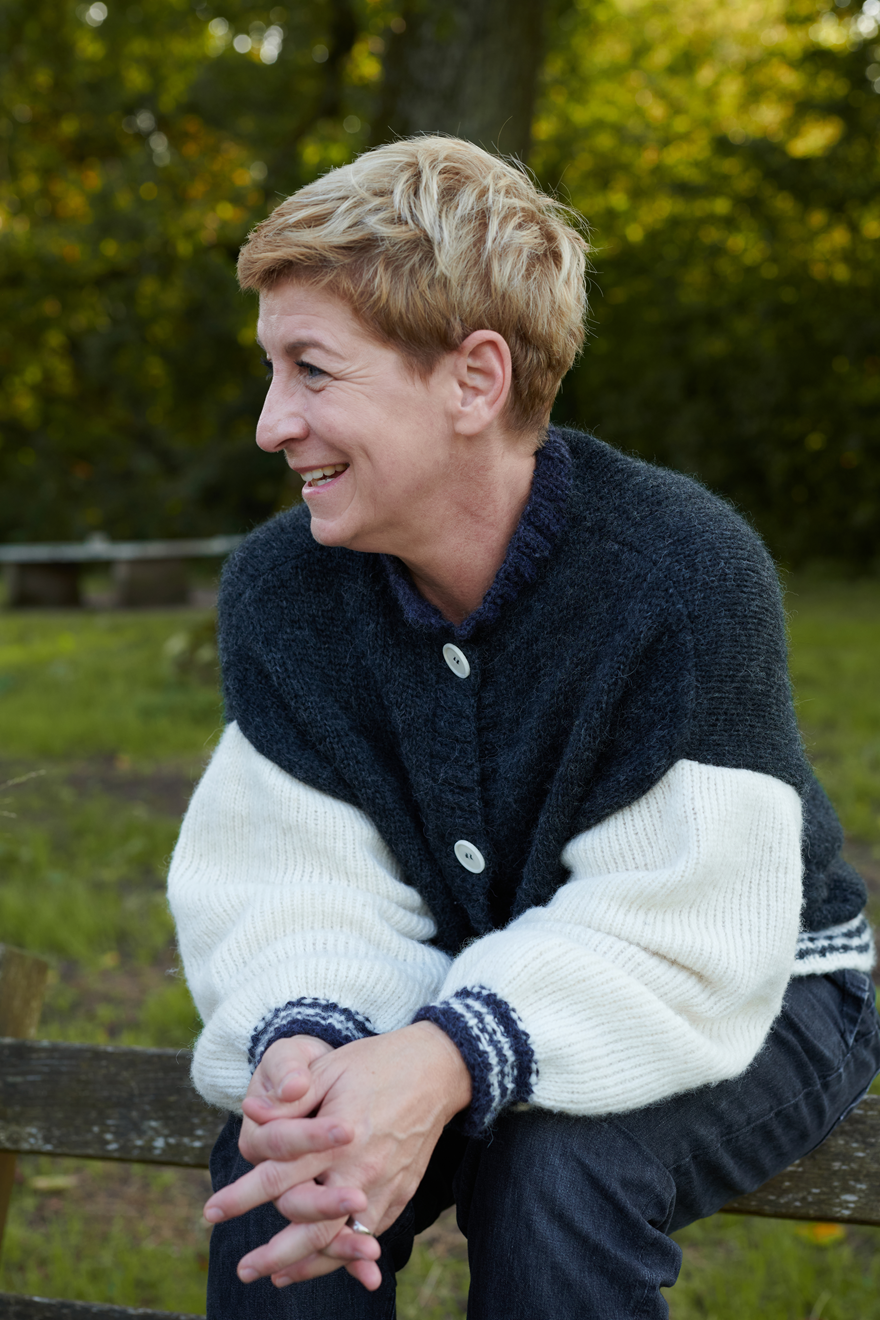 Alpaka College Cardigan VIVIAN an Model auf Bank sitzend in der Farbe natur anthrazit
