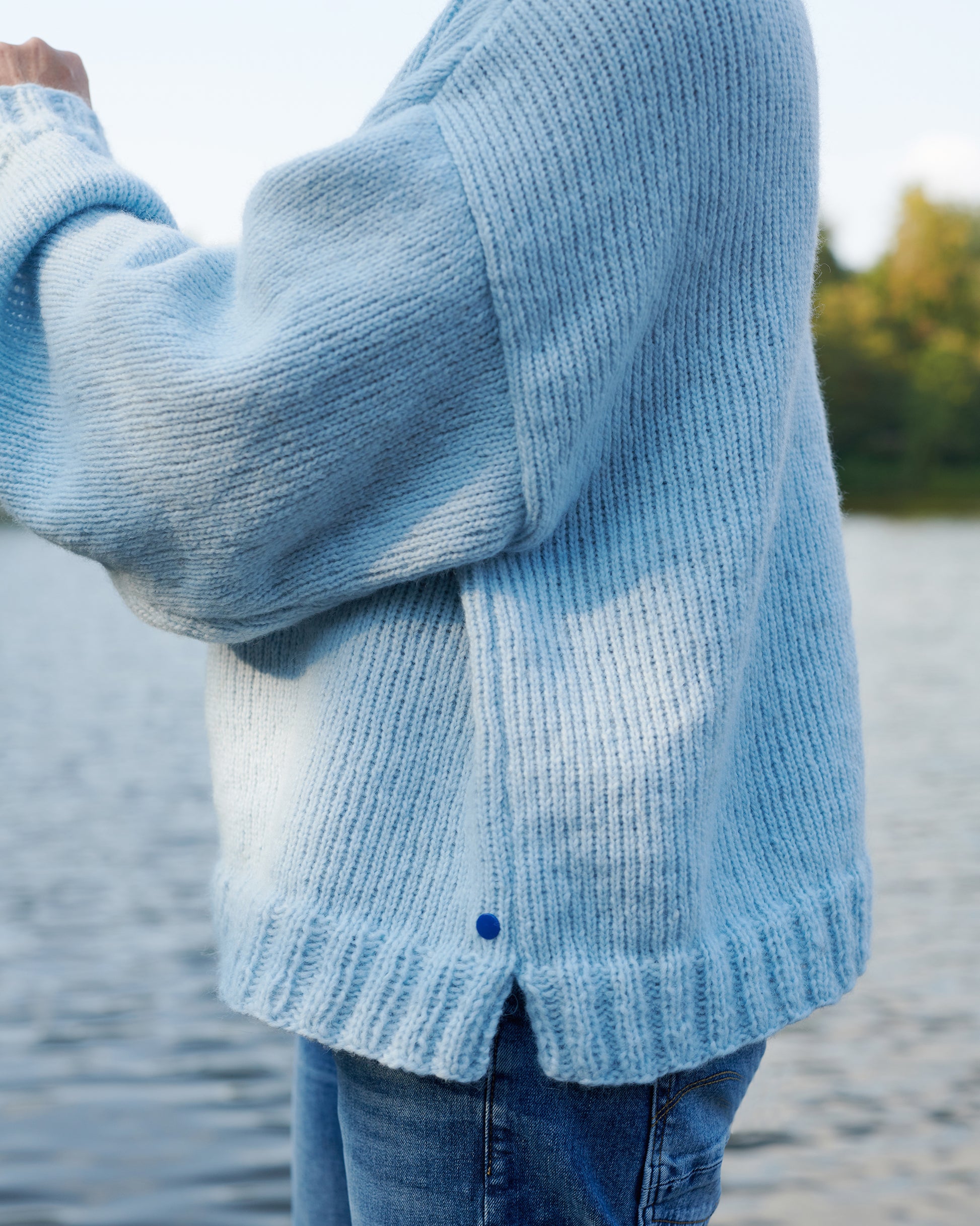 Alpaka Pullover HEIDI Detailansicht Seitennaht, Schlitz und Buendchen an Model am See in der Farbe morgennebel