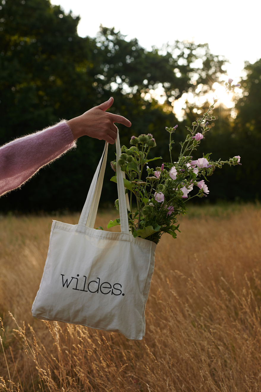 Baumwolltasche TINI mit Trägern hängend an Hand mit Blumen