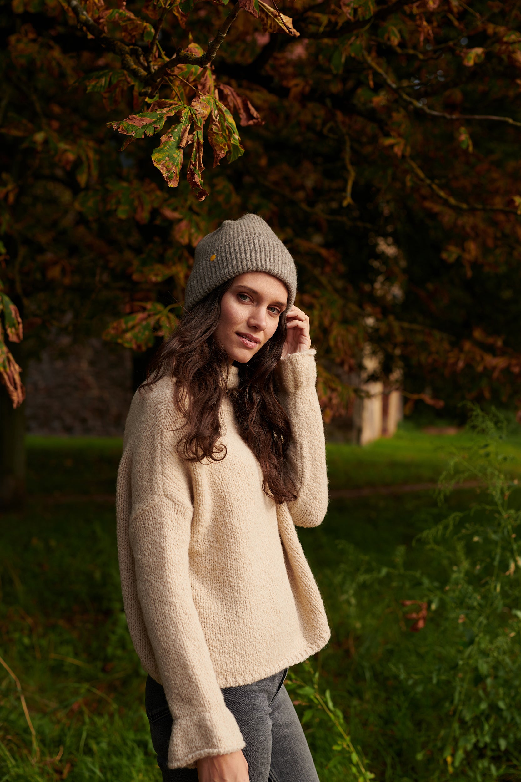 Boucle Pullover BOBBY mit halsfernem Stehkragen und Rueschenabschluss an Aermel Seitenansicht mit Muetze an Model in der Farbe natur