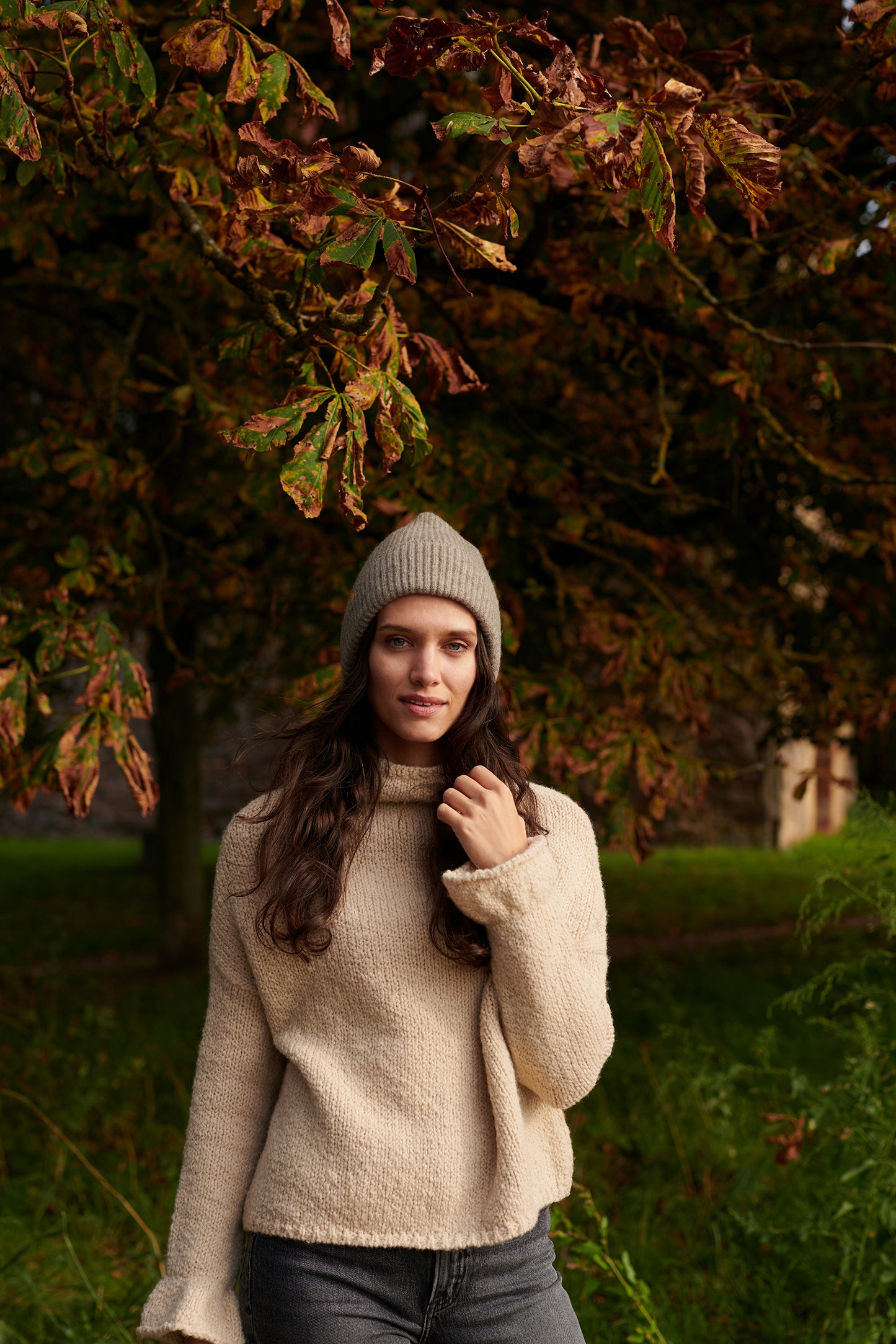 Boucle Pullover BOBBY mit halsfernem Stehkragen und Rueschenabschluss an Aermel Vorderansicht mit Muetze an Model in der Farbe natur