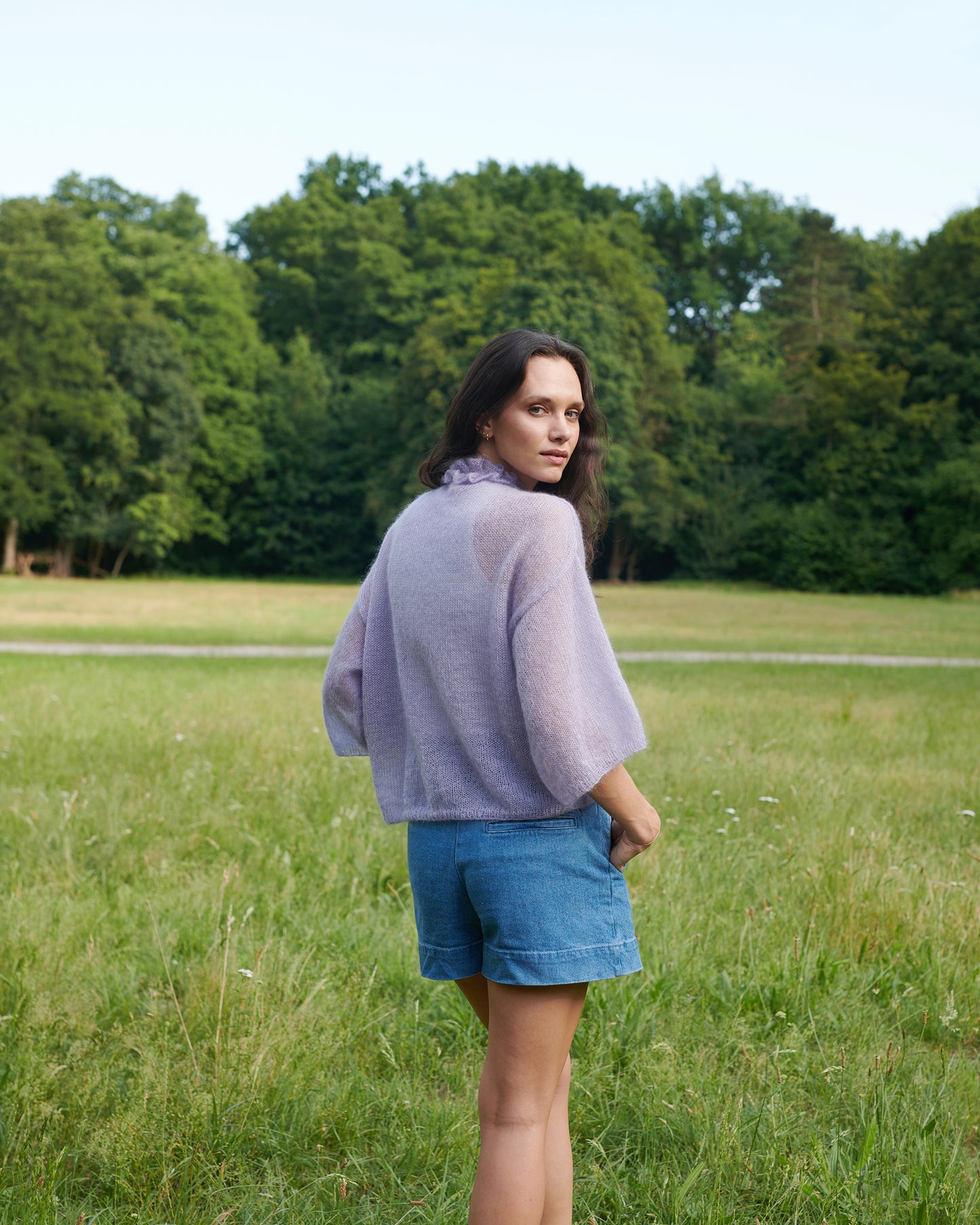 Mohair Seide Pullover FRIDA mit Rueschenkragen und Schlitz Rückansicht an Model in Wiese in der Farbe lila nebel.