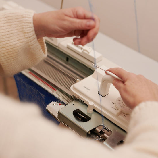Eva Wilde-Gräf von wildes. produziert an einer von Hand geführten Strickmaschine, sie führt den Faden durch den Schlitten.