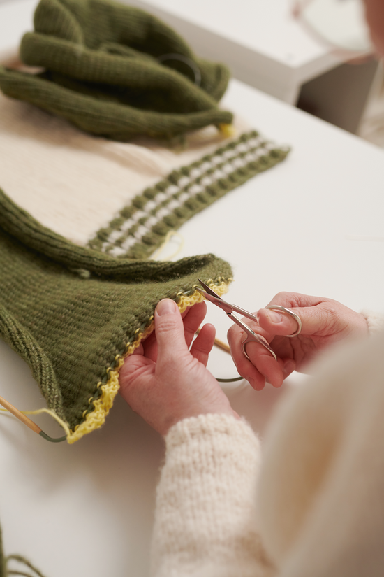 Zwei Hände schneiden den Hilfsfaden während der Fertigung  des wildes. Slowfashion Collegecardigan VIVIAN durch